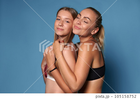 Happy young pretty woman mother in underwear, with perfect clean flawless glowing skin, hugging her adolescent daughter Happy young pretty woman mother in underwear, with perfect clean flawless glowing skin, hugging her adolescent daughter 105158752