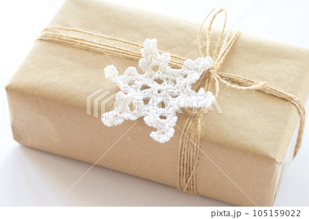 Christmas and New Year background. Gift box wrapped in kraft paper with jute cord. Decorated with a crocheted snowflake 105159022