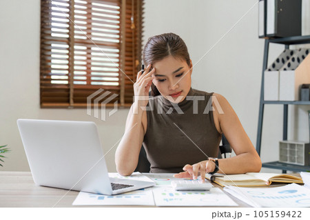 Portrait of stressed businesswoman analyzing documents in home. Asian businesswoman sitting at desk reading documents. analyzing graph working on company project 105159422