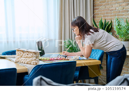 Mature woman interior designer working at her desk with fabric samples, laptop 105159574