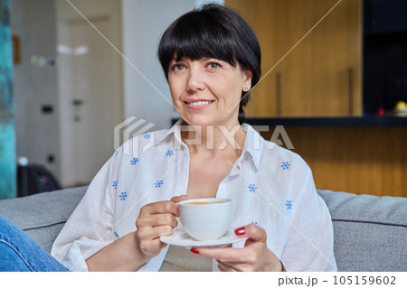 Smiling mature woman relaxing at home with cup of coffee tea 105159602