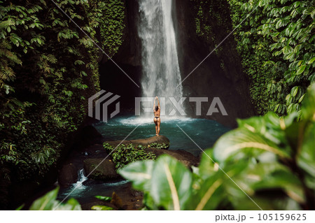 Scenic waterfall and woman in bikini. Traveler girl posing on waterfall Scenic waterfall and woman in bikini. Traveler girl posing on waterfall 105159625