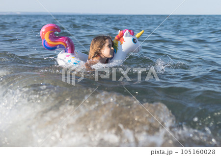 Happy baby girl swimming on an inflatable swimming unicorn in the sea Happy baby girl swimming on an inflatable swimming unicorn in the sea 105160028
