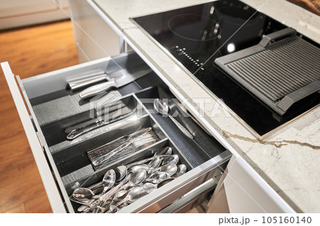 Kitchen utensil cutlery drawer organizer tray with simple set of tools, minimalist order. Open drawer with different utensils and folded towels. Order in kitchen. Kitchen furniture store. 105160140