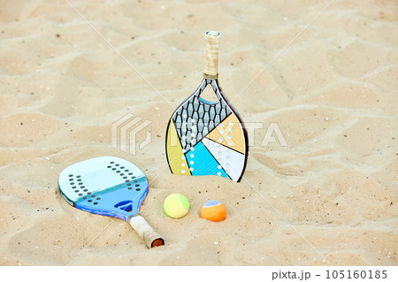 Paddle tennis racket and balls lying on sand. Summer type of game, warm outdoor training. Sport equipment Paddle tennis racket and balls lying on sand. Summer type of game, warm outdoor training. Sport equipment 105160185