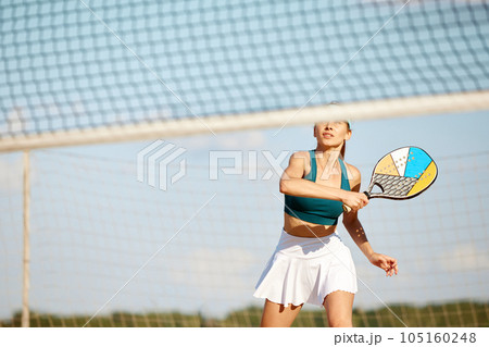 Sportive young woman playing beach, paddle tennis, hitting ball with racket. Outdoor training on warm summer day 105160248