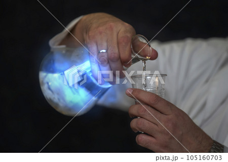 Chemical flask with a blue solution and a mystical glow in the hands of a laboratory assistant. Experiences and experiments. 105160703