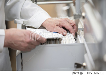 The nurse's hands are looking in the archive for a patient's card. The file is in a cell in the clinic. The nurse's hands are looking in the archive for a patient's card. The file is in a cell in the clinic. 105160732