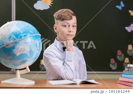A beautiful happy schoolboy is sitting at a desk A beautiful happy schoolboy is sitting at a desk 105161244