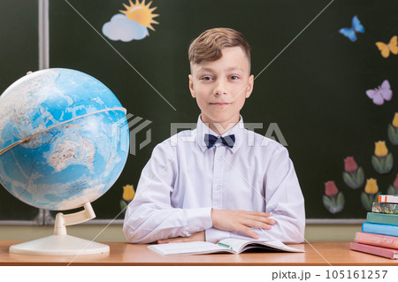 A beautiful happy schoolboy is sitting at a desk 105161257