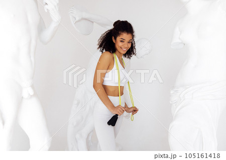 Slim young afro woman in white top and leggings with jump rope on her neck Slim young afro woman in white top and leggings with jump rope on her neck 105161418