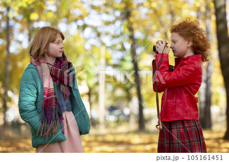Two red-haired girls girlfriends photograph each other in the autumn park with a retro camera. 105161451