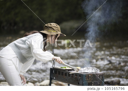 河原で真剣にバーベキューをする若い女性 105165796