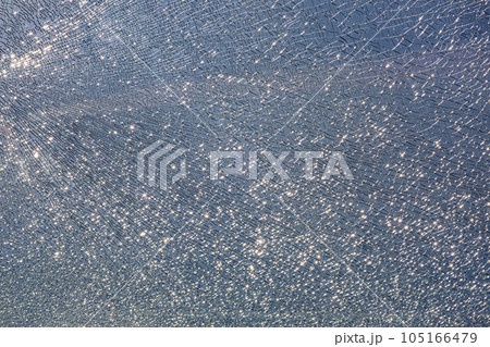 broken tempered glass in cracks, spoiled glass surface texture on blue sky background, shine from bright light, close-up. 105166479