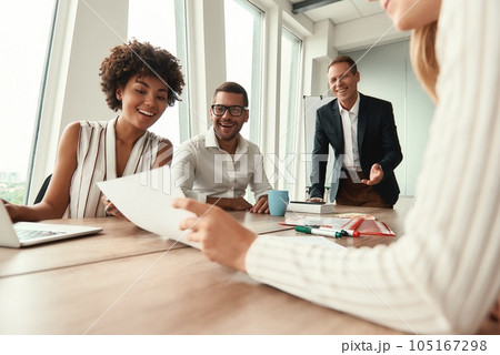 Great results Group of young business people looking at documents and smiling while sitting at the office table 105167298