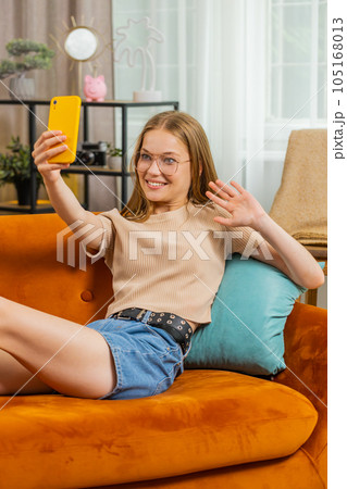 Young blonde woman taking selfie on smartphone communicating video call home online with subscribers 105168013