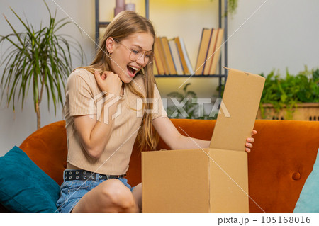 Happy young woman shopper unpacking cardboard box delivery parcel online shopping purchase at home 105168016