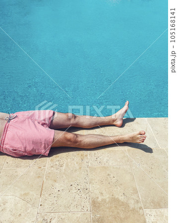 A young man lies on poolside at resort hotel during vacation. Close up of male legs near turquoise water. A young man lies on poolside at resort hotel during vacation. Close up of male legs near turquoise water. 105168141