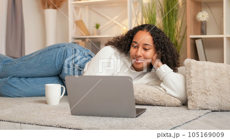 Internet entertainment. Gadget leisure. Home weekend. Satisfied cheerful woman looking laptop surfing online on floor comfortable living room. 105169009