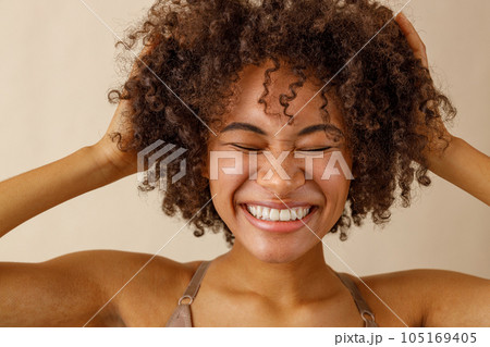Beautiful lady with curly hairstyle posing against beige wall Beautiful lady with curly hairstyle posing against beige wall 105169405