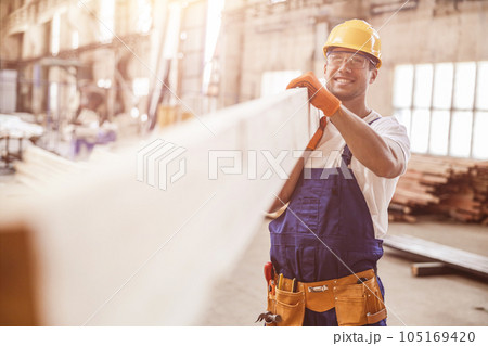 Smiling man builder carrying wooden plank at construction site 105169420