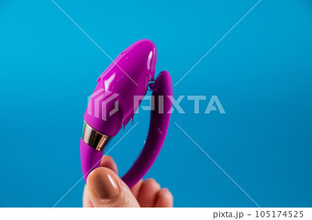 A woman holds a curved sex toy in lubrication on a blue background. Vaginally clitoral vibrator. 105174525