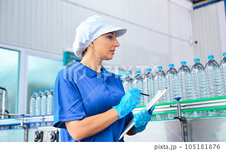 Bottling factory worker inspecting quality of water bottles before shipment. Reverse osmosis system used in plant. water purity and maintaining quality control in bottling process. High quality photo 105181876