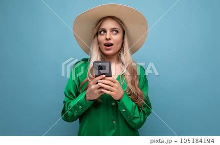 surprised young woman on vacation in a summer jute hat with a phone on a blue studio background with surprised young woman on vacation in a summer jute hat with a phone on a blue studio background with 105184194