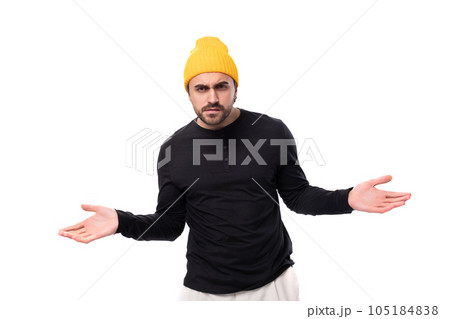 a young modest brutal male model dressed in a black jacket and a yellow hat shrugs his shoulders a young modest brutal male model dressed in a black jacket and a yellow hat shrugs his shoulders 105184838