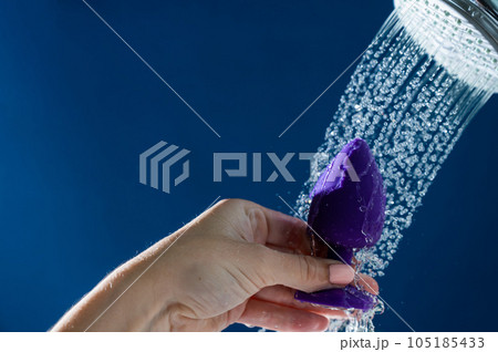 Woman washing purple anal plug under shower on blue background. Woman washing purple anal plug under shower on blue background. 105185433