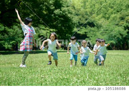 緑地でかけっこをする子供たちと、見守る女性 緑地でかけっこをする子供たちと、見守る女性 105186086