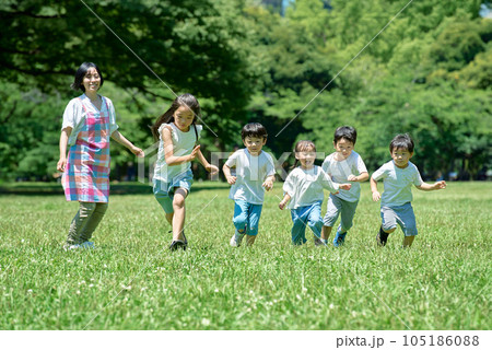 緑地でかけっこをする子供たちと、見守る女性 緑地でかけっこをする子供たちと、見守る女性 105186088