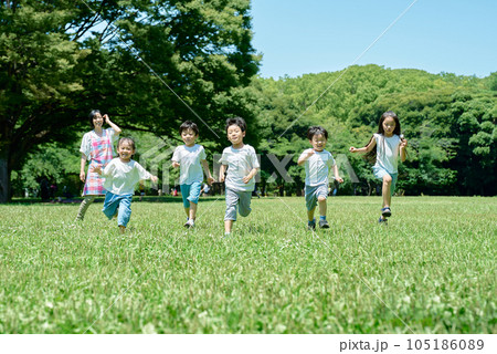 緑地でかけっこをする子供たちと、見守る女性 緑地でかけっこをする子供たちと、見守る女性 105186089