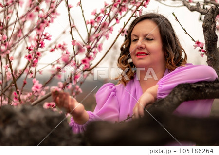 Woman peach blossom. Happy curly woman in pink dress walking in the garden of blossoming peach trees in spring 105186264