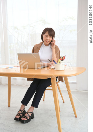 部屋の机でスマホで電話する女性 105186546