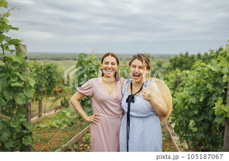 happy beautiful women in elegant dresses and wide brimmed straw hats are smiling and looking at the camera 105187067
