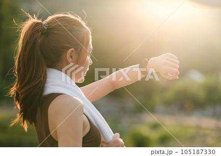 Healthy woman relax after cool down and looking smart watch for check timing run. Woman workout after fitness and jogging session at the park. Healthy and Lifestyle Concept. 105187330