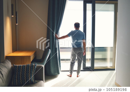 Young man in casual clothes opens curtain window in early morning. 105189198