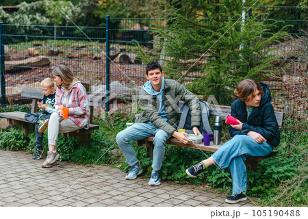 Happy Family drinking tea from a thermos in the forest. Photo of cute charming mother with childrens dressed casual outfit walking sitting bench drinking tea smiling outside city park 105190488