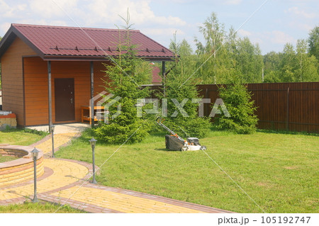 Lawn mower on a sloping green lawn yard of a country house, Russia. Backyard of the house. Lawn mower on a sloping green lawn yard of a country house, Russia. Backyard of the house. 105192747