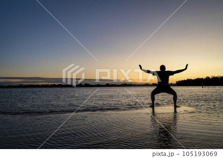 sunrise silhouette of a man standing in shallow water and practicing chigong or tai chi movements, Boyd Lake State Park in northern Colorado sunrise silhouette of a man standing in shallow water and practicing chigong or tai chi movements, Boyd Lake State Park in northern Colorado 105193069