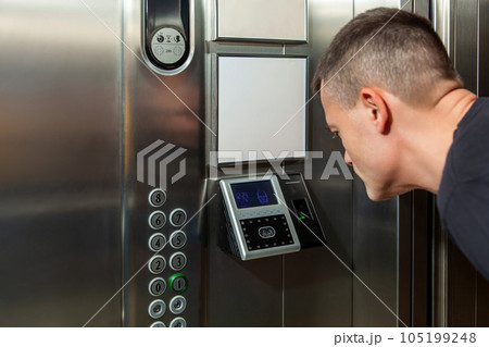 A man shows his face to a fingerprint access control terminal with a facial recognition function installed in the elevator 105199248