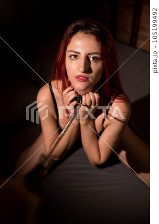 Leather belt on the neck of BDSM. Luxurious chest in black underwear. A woman kneels in sexual games as a victim. Toys for adults. 105199492