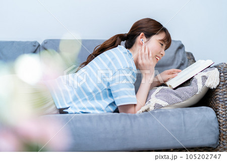 ソファに寝転んで音楽を聴きながら本を読む女性 ソファに寝転んで音楽を聴きながら本を読む女性 105202747