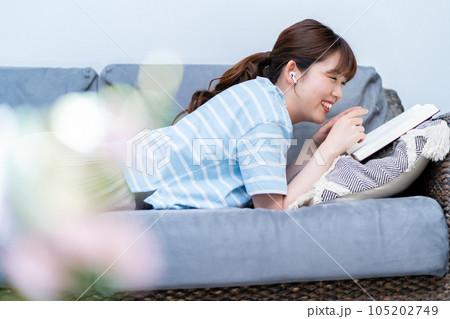 ソファに寝転んで音楽を聴きながら本を読む女性 ソファに寝転んで音楽を聴きながら本を読む女性 105202749