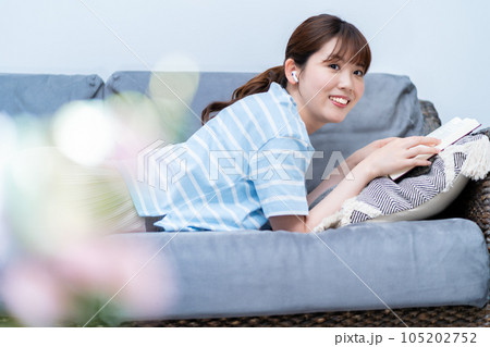 ソファに寝転んで音楽を聴きながら本を読む女性 ソファに寝転んで音楽を聴きながら本を読む女性 105202752