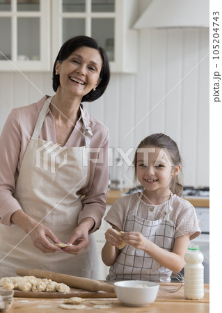 Cheerful grandmother and sweet kid girl in aprons baking dessert Cheerful grandmother and sweet kid girl in aprons baking dessert 105204743