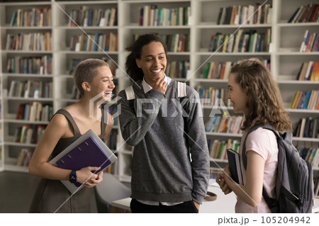 Cheerful diverse student girls and guy talking in college library Cheerful diverse student girls and guy talking in college library 105204942