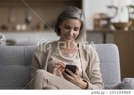 Cheerful beautiful mature woman using application on smartphone Cheerful beautiful mature woman using application on smartphone 105204969