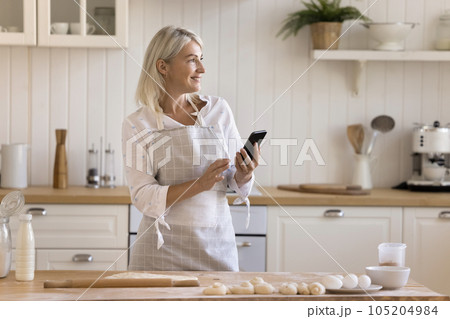 Happy pretty blonde mature housewife in apron browsing cooking recipe 105204984